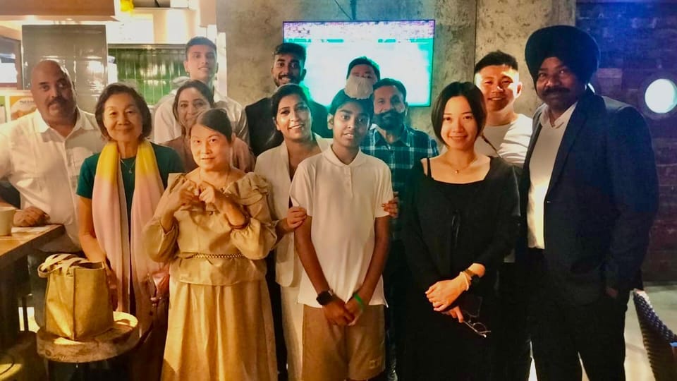 A group of men and women stand close together for a photograph in a café, one of them making a heart shape with both hands.